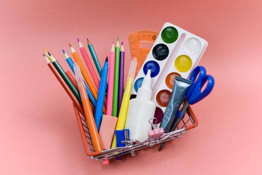 School supplies in a shopping basket on a pink background. Preparing for school, buying office supplies. Back to school.