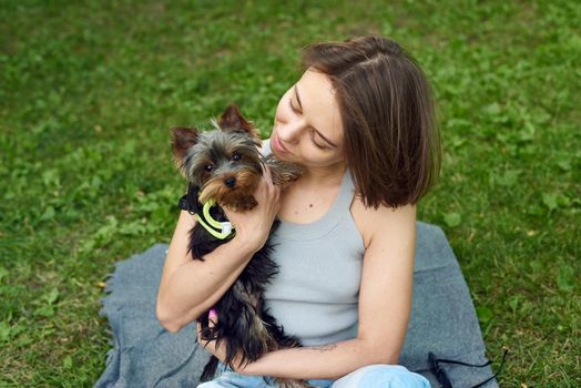 Cute beautiful woman with little Yorkshire Terrier in a park outdoors. Lifestyle portrait.