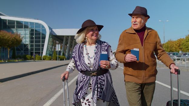 Senior couple happy pensioner tourists grandmother grandfather stay with luggage suitcases, tickets, passports from international airport hall or railway station. Travel, vacation, journey, trip