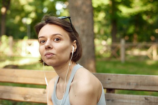 Beautiful young brunette hipster woman listening music in the park on the bench. Pretty woman in the park listening music.