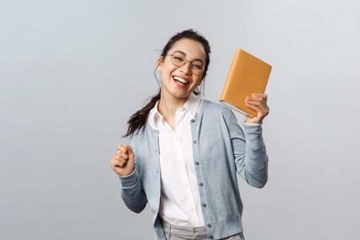 Education, teachers, university and schools concept. Cheerful carefree, smiling asian female student celebrating end of semester, dancing with planner or notebook, smiling rejoicing.