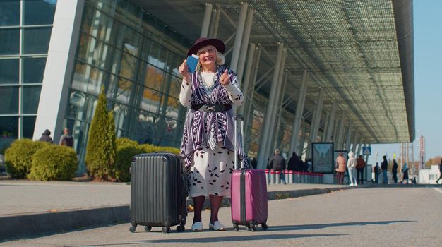 Senior pensioner one tourist grandmother businesswoman stay near international airport or railway station with luggage celebrate success win rejoices doing winner gesture. Travel, vacation, holidays
