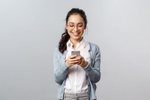 Office lifestyle, business and people concept. Happy cheerful korean woman texting friend, use mobile phone, smiling at smartphone display as having funny conversation, watch video online.