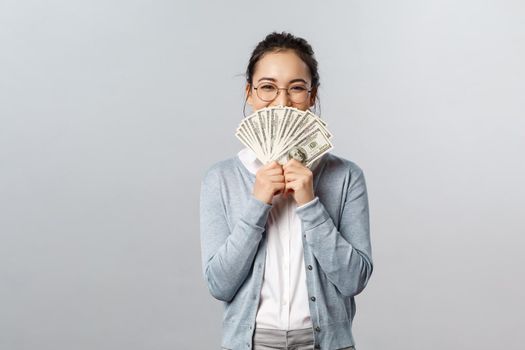 Business, finance and investment concept. Cheerful laughing asian female holding money dollars hiding smile behind cash as celebrating award, receive prize, winning lottery, become rich.