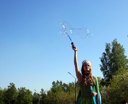 A beautiful girl in a butterfly costume and a crown blows soap bubbles. Carnival..