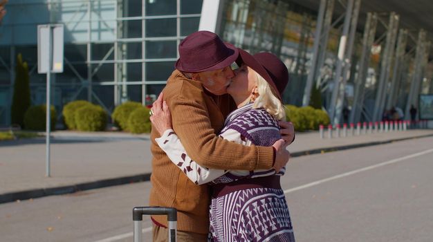 Senior old grandmother grandfather retirees tourists reunion in airport terminal after long separation traveling. Lovely senior couple husband and wife happily hugging meeting after business trip