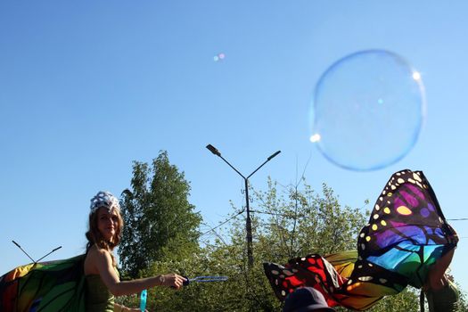 A beautiful girl in a butterfly costume and a crown blows soap bubbles. Carnival..