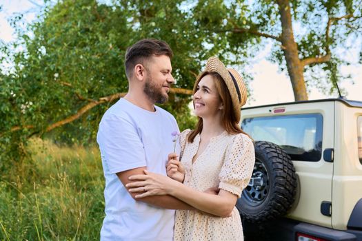 Love and romance of middle-aged couple. Happy hugging man and woman near car, summer nature wild meadow background. Relationship, holiday, date, trip, journey, weekend, family, people 40s concept