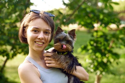 A cute girl with a square hugs a Yorkshire terrier on the street. Hugs with your little dog in the park.