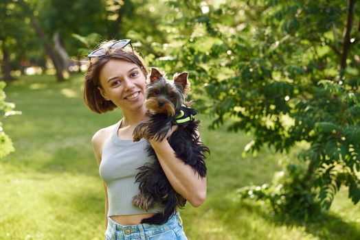 Cute beautiful woman with little Yorkshire Terrier in a park outdoors. Lifestyle portrait.