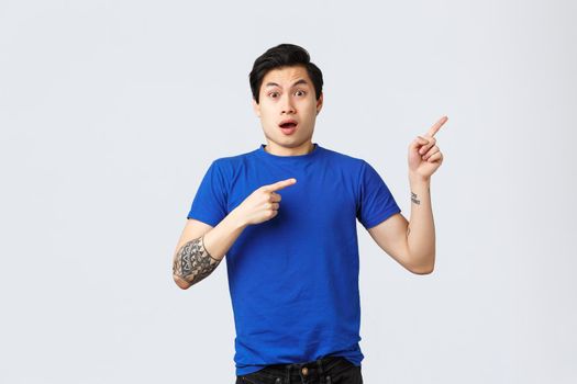Different emotions, people lifestyle and advertising concept. Shocked and nervous young asian man in blue t-shirt pointing fingers upper right corner. Gasping guy showing exciting news.