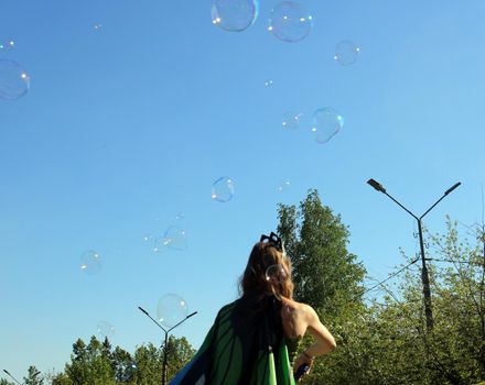 A girl in a colorful butterfly costume blows soap bubbles. Carnival..