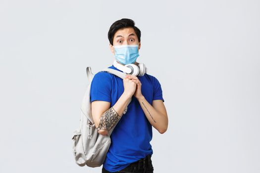 Back to school, studying on covid-19, education and university life concept. Nervous young asian guy in medical mask, student freshman feel worried first day college, wear medical mask and backpack.