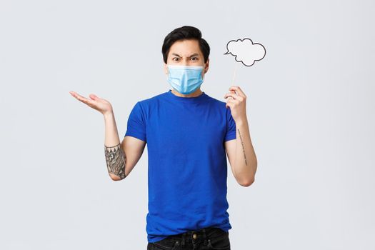 Lifestyle, people different emotions and covid-19 pandemic concept. Angry man in medical mask swearing and complaining, raise hand dismay, grimacing, holding comment cloud near head.