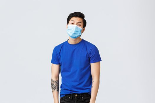 Different emotions, social distancing, self-quarantine on coronavirus and lifestyle concept. Tired and bored asian man in medical mask, guy dying of boredom staying home during covid-19.
