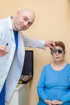 A male optometrist checks the eyesight of an adult woman with a trial frame.