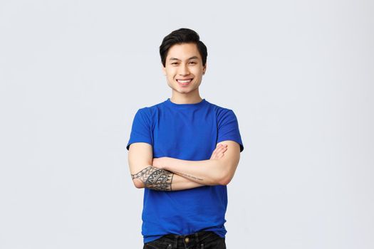 Young carefree asian guy in blue t-shirt, cross arms chest determined and ready to work, smiling enthusiastic, being in good mood, self-quarantine, social distancing home during covid-19.