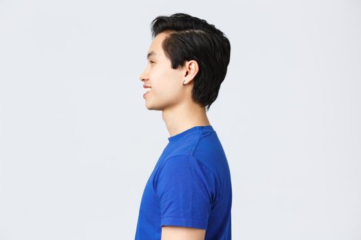 Lifestyle, people emotions and beauty concept. Profile shot of asian hipster guy with earring in blue t-shirt, smiling satisfied after making good new hairuct, hairstyle at barbershop.