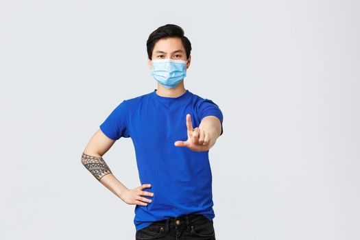 Different emotions, social distancing, self-quarantine on covid-19 and lifestyle concept. Serious determined asian man telling to stop, show finger to forbid or scold someone, wear medical mask.