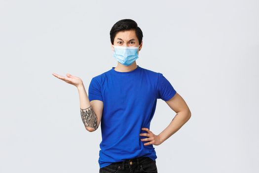 Different emotions, social distancing, self-quarantine on covid-19 and lifestyle concept. Angry complaining male customer, asian guy in medical mask pointing hand left and frowning disappointed.