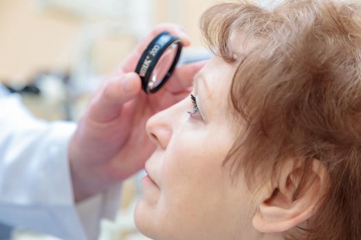 A male ophthalmologist checks the eyesight of an adult woman with a binocular ophthalmoscope.