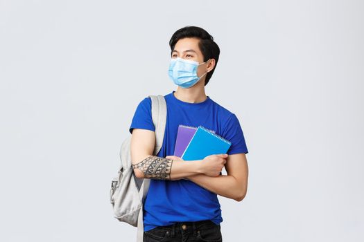 Back to school, studying during covid-19, education and university life concept. Carefree handsome asian male student, college freshman in medical mask with notebooks and backpack.