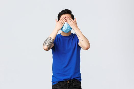 Different emotions, social distancing, self-quarantine on covid-19 and lifestyle concept. Asian man in blue t-shirt and medical mask standing blindfolded, cover eyes not see what happening.