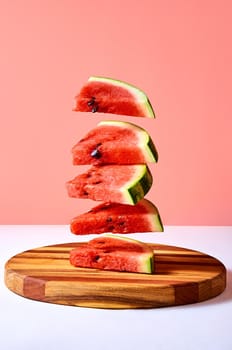 Fresh ripe pieces watermelon flying over wooden board on pink background. Creative minimal concept.