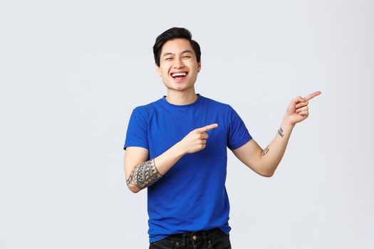 Different emotions, people lifestyle and advertising concept. Attractive cheerful queer asian man celebrating pride month, pointing fingers right at banner. Smiling guy introduce or recommend product.