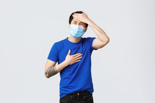 Different emotions, social distancing, self-quarantine on coronavirus and lifestyle concept. Sick young asian man with covid-19, touching lungs or heart and forehead, have high fever, flu symptoms.