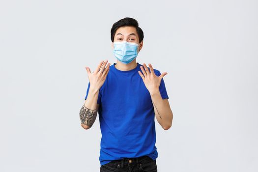 Different emotions, social distancing, self-quarantine on coronavirus and lifestyle concept. Happy and excited asian man in medical mask shaking hands, express cheer over good surprise news.