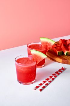 Fresh watermelon juice or smoothie in glasses with watermelon pieces on wooden board on pink background. Refreshing summer drink. Vertical orientation