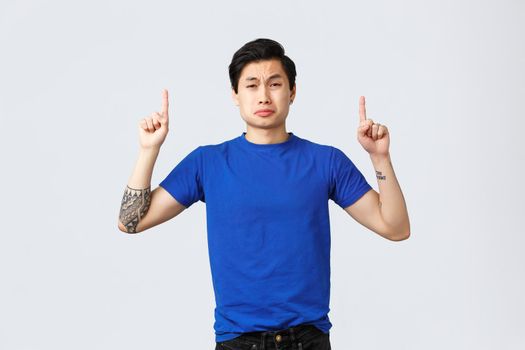 Different emotions, people lifestyle and advertising concept. Desperate and sad young grieving asian man in blue t-shirt, sobbing and whining, complaining and pointing fingers up.