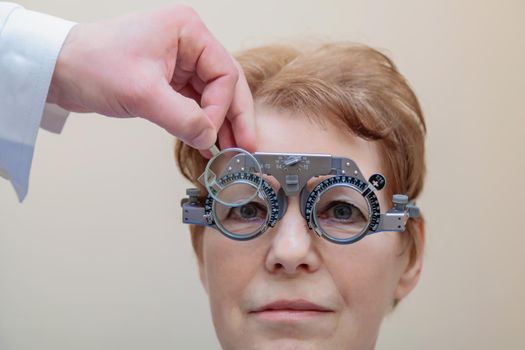 A male optometrist checks the eyesight of an adult woman with a trial frame.