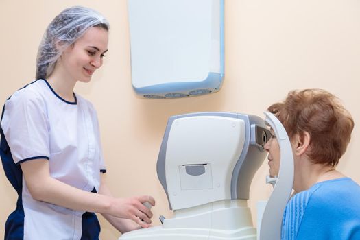 A girl optometrist examines the eyes of a patient using special modern equipment.
