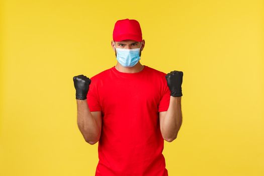 Express delivery during pandemic, covid-19, safe shipping, online shopping concept. Determined courier in red uniform, medical mask and gloves, ready to carry your packages, feel strong.
