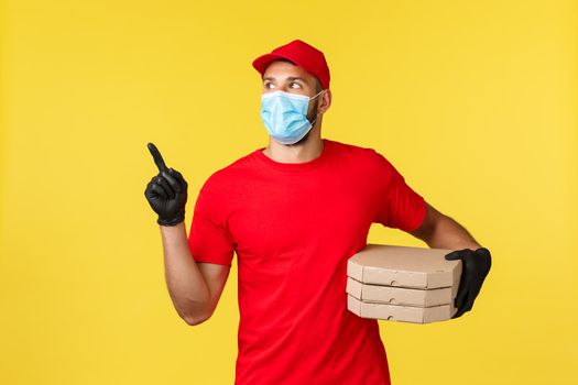 Food delivery, tracking orders, covid-19 and self-quarantine concept. Young courier searching house to deliver pizza to client, look left, wear red uniform and protective personal equipment.