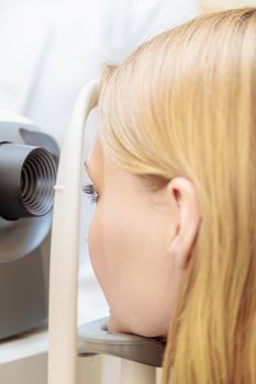 A young girl at the reception at the ophthalmologist checks her eyesight on a special apparatus. Close-up.