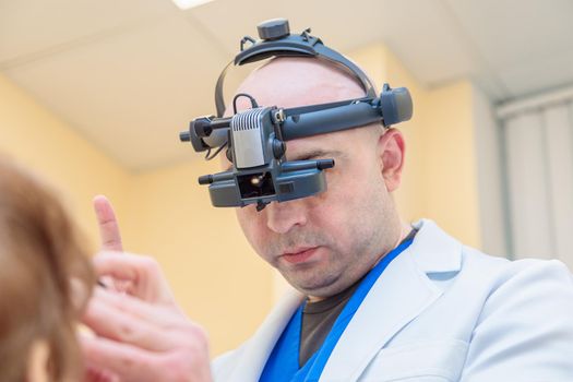 A male ophthalmologist checks the eyesight of an adult woman with a binocular ophthalmoscope.