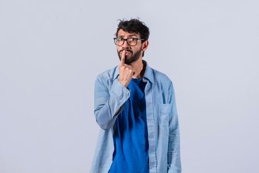 pensive young man with his finger on his lips on an isolated background, a pensive guy with a finger on his lips, pensive man on an isolated background