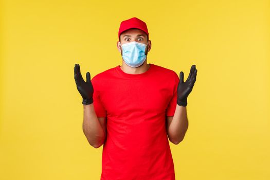 Express delivery during pandemic, covid-19, safe shipping, online shopping concept. Impressed and startled courier in red uniform cap, t-shirt raise hands astonished, wear medical mask.