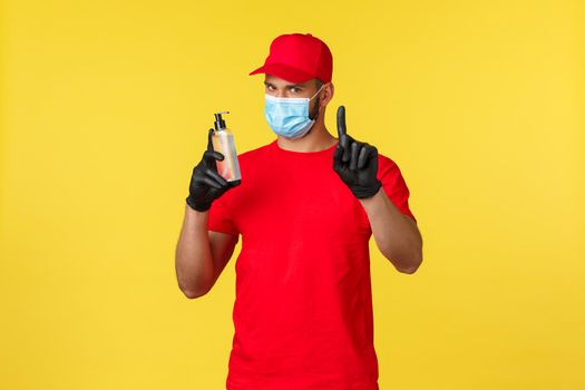 Covid-19, delivery orders, shopping, contactless handling and social distancing concept. Serious courier in medical mask and gloves tell to use hand sanitizer for preventing catching coronavirus.