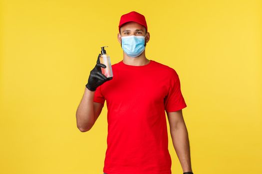Covid-19, delivery orders, shopping, contactless handling and social distancing concept. Enthusiastic courier in red uniform, medical mask and gloves, recommend use hand sanitizer, smiling.