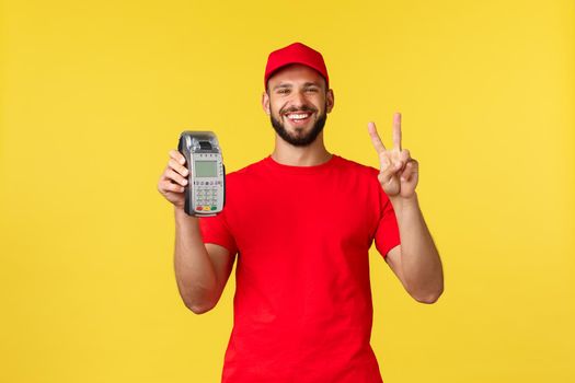 Contactless payment, online delivery, internet shopping and parcel tracking concept. Funny friendly courier in red uniform cap and t-shirt, employee make peace sign and show POS terminal.