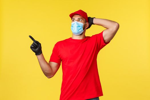 Express delivery during pandemic, covid-19, safe shipping, online shopping concept. Shocked and impressed courier in red uniform, medical mask and gloves, point and staring upper left corner.