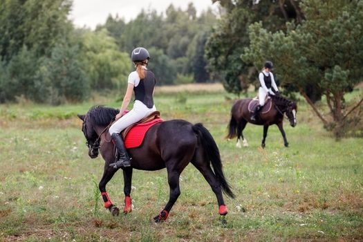 Two Jockey girl doing horse riding on countryside meadow. Horse riding, training and rehabilitation.