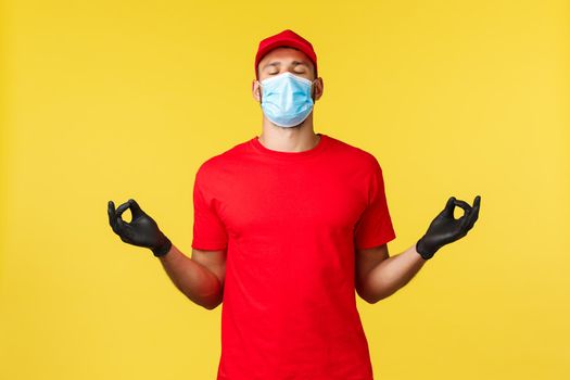 Express delivery during pandemic, covid-19, safe shipping, online shopping concept. Peaceful and patient courier in red uniform and medical mask, meditating, stay calm working, yellow background.
