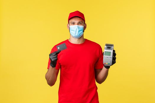 Food delivery, tracking orders, covid-19 and self-quarantine concept. Courier in red uniform, medical mask and gloves, showing POS terminal and credit card, contactless paying during coronavirus.