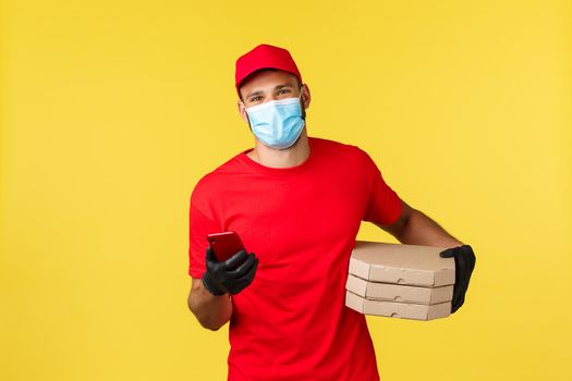 Food delivery, tracking orders, covid-19 and self-quarantine concept. Friendly smiling courier in red uniform, employee using smartphone to call client bring pizza orders, using application on phone.