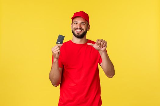 Contactless payment, online delivery, internet shopping concept. Handsome young bearded male courier in red uniform cap and t-shirt, hold credit card and pointing at it pleased.